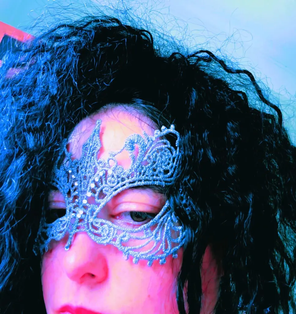 AmberCrystalZone wears a silver lace mask over her eyes, framing her dark, curly hair and face.