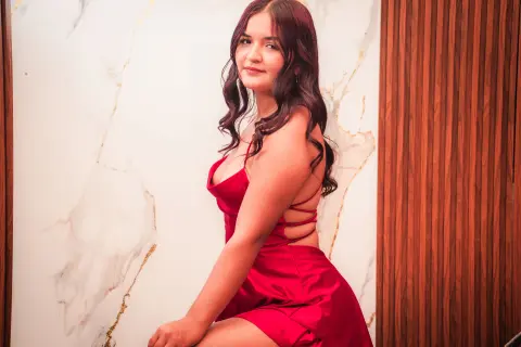 Smiling young woman in a red satin dress posing against a marble and wood paneled wall.