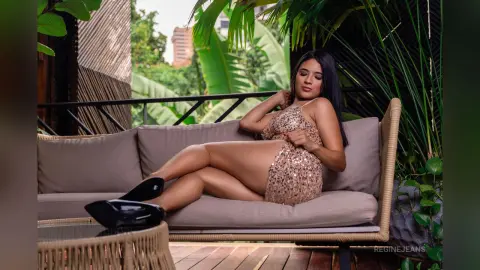 RegineJeans sits on a patio couch wearing a sparkly gold mini dress that shows off her long legs.
