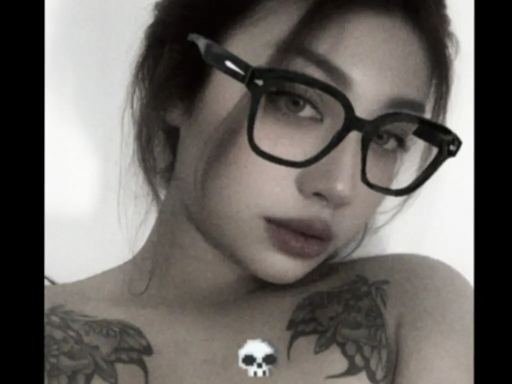 Portrait of a tattooed woman wearing black glasses with a moody, aesthetic vibe.