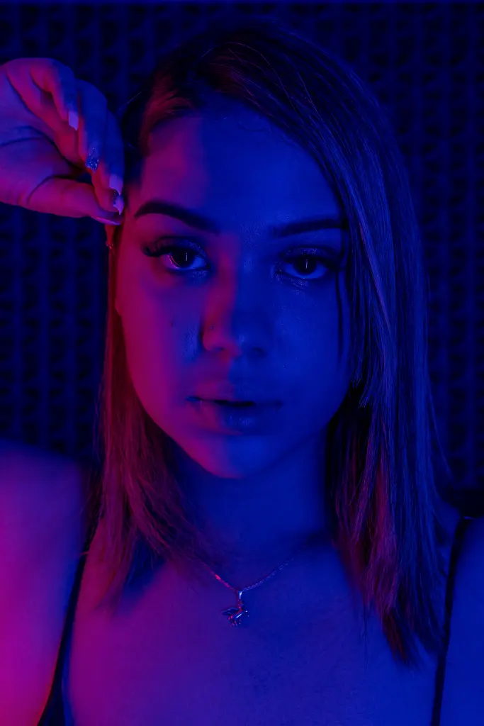 Amber_Duran — Young woman in a black tank top under moody blue and pink neon lighting for a cinematic portrait.