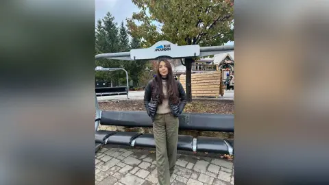 Woman in a black puffer jacket and olive trousers standing outdoors at Blue Mountain resort on an autumn day.