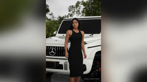 Elegant woman in a sleek black midi dress posing confidently in front of a white luxury SUV outdoors.