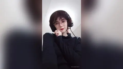Young woman with glasses and headphones wearing a black turtleneck in a minimalist indoor setting.