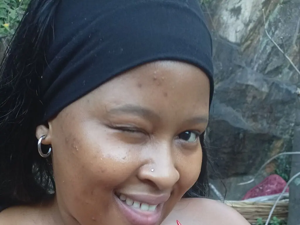 Smiling young woman with a black headband and silver hoop earrings in a natural outdoor setting.