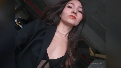 Young woman in a black blazer and necklace posing with a confident expression in a modern indoor setting.