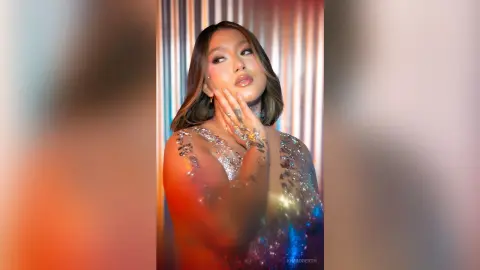 KimRoberth poses in a shimmering silver glitter dress with her hand touching her face against a striped background.