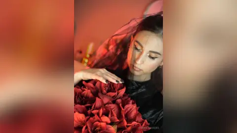 Elegant woman in a black dress holding a bouquet of red flowers under a romantic red veil.