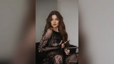 Elegant woman in a black lace sheer dress posing with a moody, sophisticated look in a minimalist studio setting.