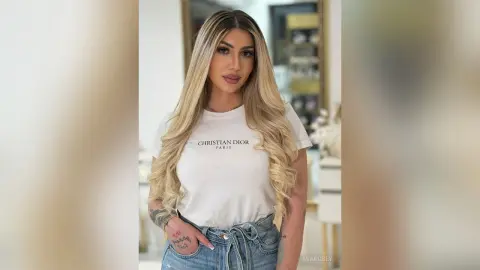 Blonde woman in a white Christian Dior t-shirt and denim jeans posing in a bright, modern room.