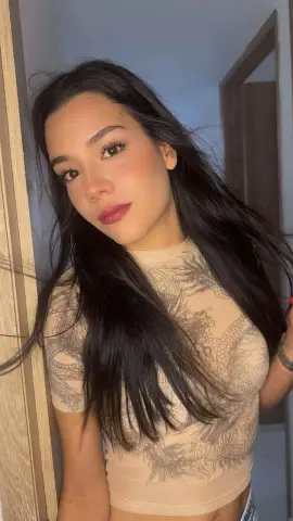 Young woman with long dark hair wearing a beige patterned mesh crop top in a bright indoor setting.