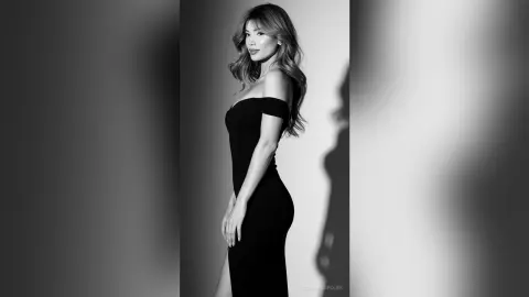 Elegant woman in a sleek black off-the-shoulder dress posing for a moody black and white studio portrait.