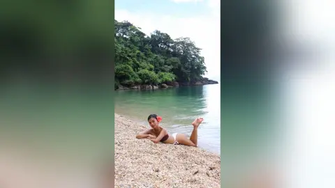 Relaxed woman in a dark bikini relaxing on a tropical pebble beach by turquoise ocean water.