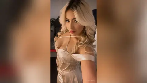 Blonde woman in a glamorous white satin dress posing with a soft, elegant mood in a modern indoor setting.