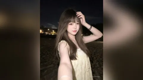 TessaMabel — TessaMabel poses outdoors at night wearing a yellow floral sundress with her hand in her long brown hair.