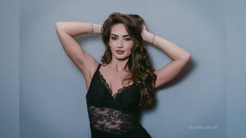 Elegant woman in a black lace cocktail dress posing against a grey studio background with a glamorous mood.