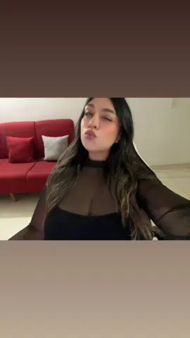 Playful young woman in a black sheer top making a pouty face while sitting in a cozy living room.