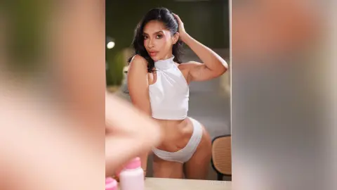 LucyMartin poses in a white halter-neck crop top and matching white bottoms, running her hand through her dark hair.