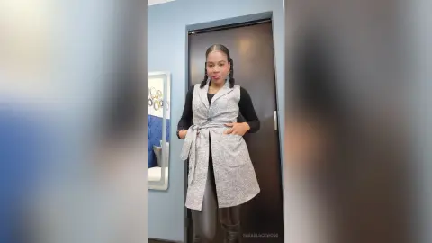 Stylish woman in a grey longline vest and black top standing in a modern minimalist room.