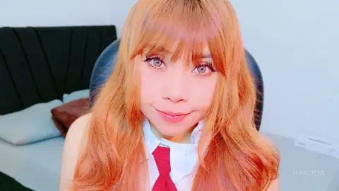 HimeJess smiles at the camera wearing a white shirt and red tie with long, wavy orange hair.