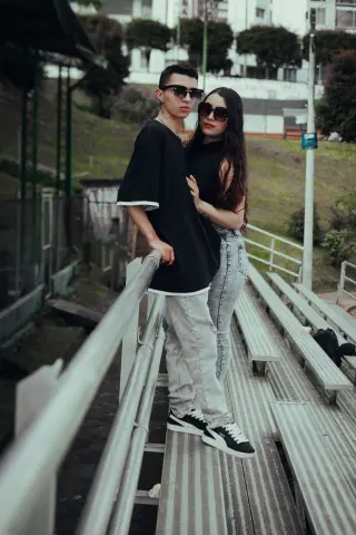 Trendy young couple in black t-shirts and light denim posing on outdoor bleachers with a relaxed urban mood.