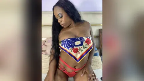 KattyLeya — KattyLeya sits on a bed wearing a blue floral bandeau top and red strappy bikini bottoms.