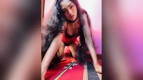 Young woman with long wavy hair in a red outfit posing on a rug with a moody, dramatic aesthetic.