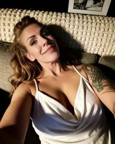Smiling woman in a white camisole relaxing on a cozy textured sofa in warm indoor lighting.