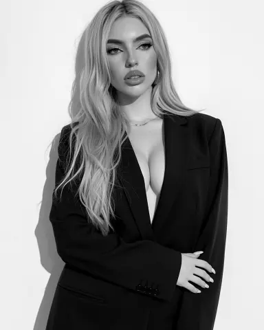 Glamorous blonde woman in a black blazer posing against a white background in a chic studio portrait.