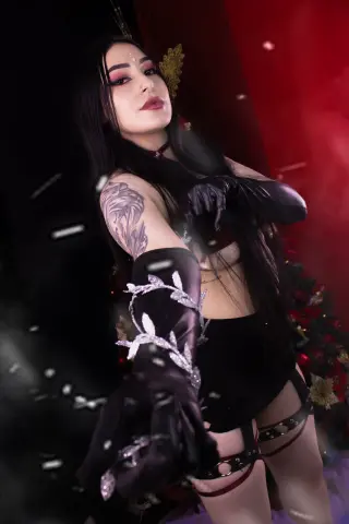 Gothic woman in black lace gloves and dark outfit posing in a moody, red-lit mystical setting.
