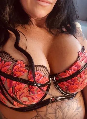 SensationalMya77 wears a floral red and black lace bra that highlights her large breasts and cleavage.