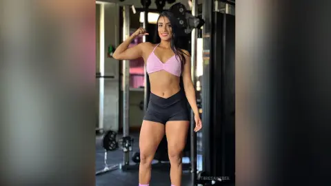 Smiling athletic woman in pink sports bra and black shorts posing in a gym setting.