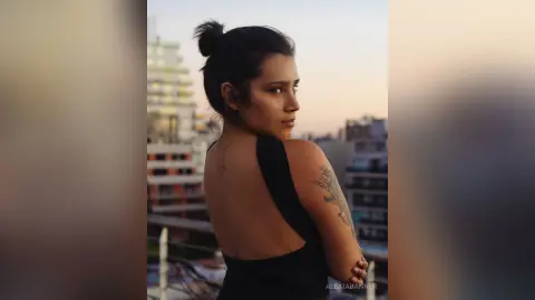 Young woman in a black backless dress looking over her shoulder on a city rooftop at sunset.