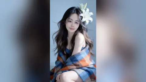 Elegant woman with long dark hair and a white flower accessory wrapped in a cozy blue and orange plaid blanket.