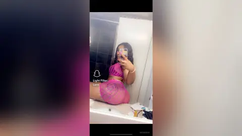 Young woman in pink lace lingerie taking a mirror selfie in a modern bathroom.