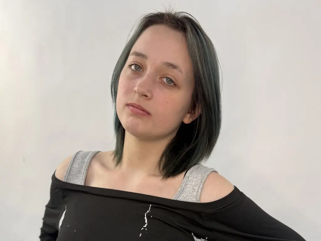 SoleneWinter poses with her short, dark hair and light eyes, wearing a black off-the-shoulder top against a plain white background.