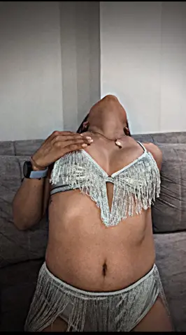 Woman in a silver sequin fringe bikini set relaxing on a grey sofa in a bright indoor setting.