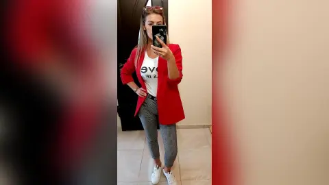 Stylish woman in a red blazer and white graphic t-shirt posing for a mirror selfie in a modern room.