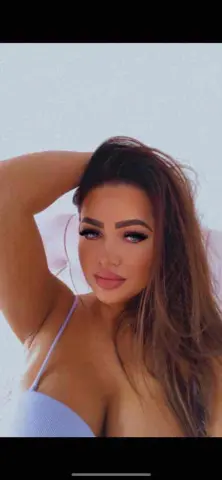 Assyya — Assyya poses with her hand in her hair, wearing a light purple bra top.
