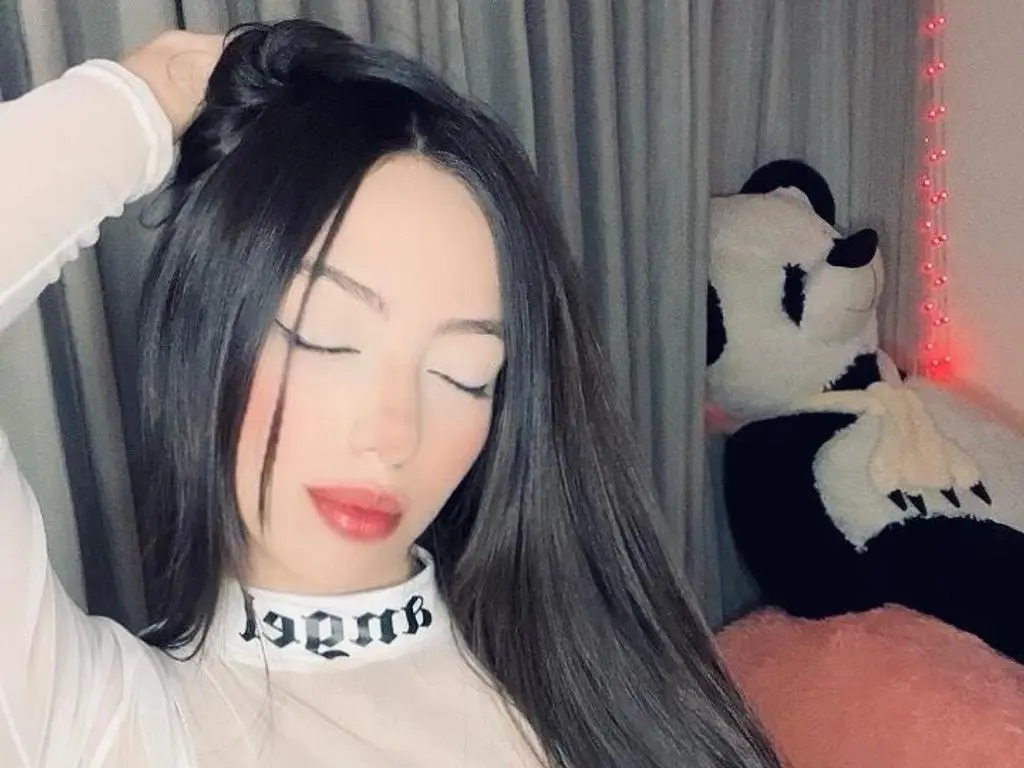 AriaFoxx poses with her eyes closed, wearing a white long-sleeve mesh top and showing off her long, straight black hair.