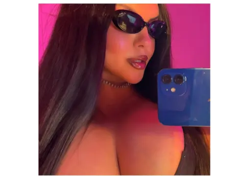 PrincesssAnisia — PrincesssAnisia wearing black sunglasses and a choker, posing for a selfie against a pink background.