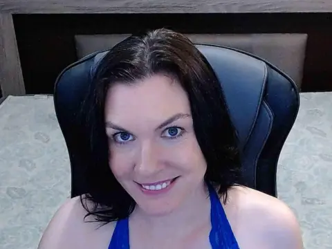 Smiling brunette woman in a blue top sitting in a black office chair in a bright room.