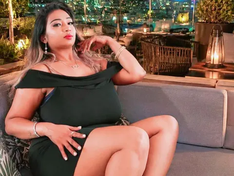 princesSsandy — princesSsandy sits on an outdoor sofa wearing a black off-the-shoulder dress with city lights in the background.