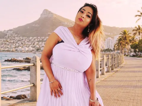 princesSsandy — princesSsandy poses in a light purple dress on a seaside walkway with mountains in the background.