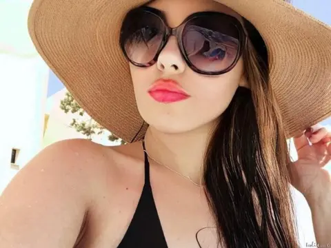 EvaHarris — Young woman in black bikini and wide-brimmed sun hat wearing sunglasses on a sunny summer day.