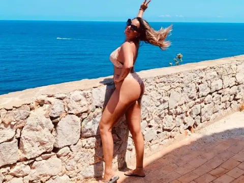 kitttty4play — Happy woman in a beige bikini posing by a stone wall overlooking the blue ocean on a sunny summer day.