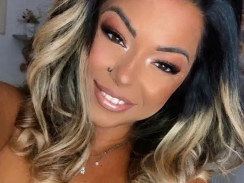 kitttty4play — Smiling woman with blonde highlighted wavy hair and glamorous makeup wearing a delicate silver necklace.