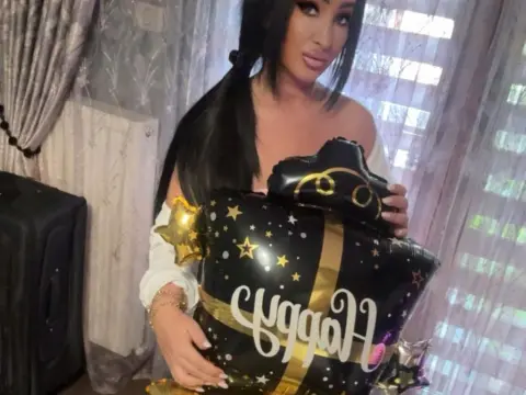 Smiling woman in a white top holding a black and gold Happy Birthday balloon in a bright room.