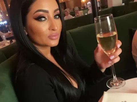 Glamorous woman in a black outfit holding a champagne glass at an upscale evening lounge.