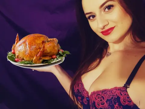 Annastea21x — Smiling woman in a lace bra holding a large roasted turkey platter against a dark purple background.